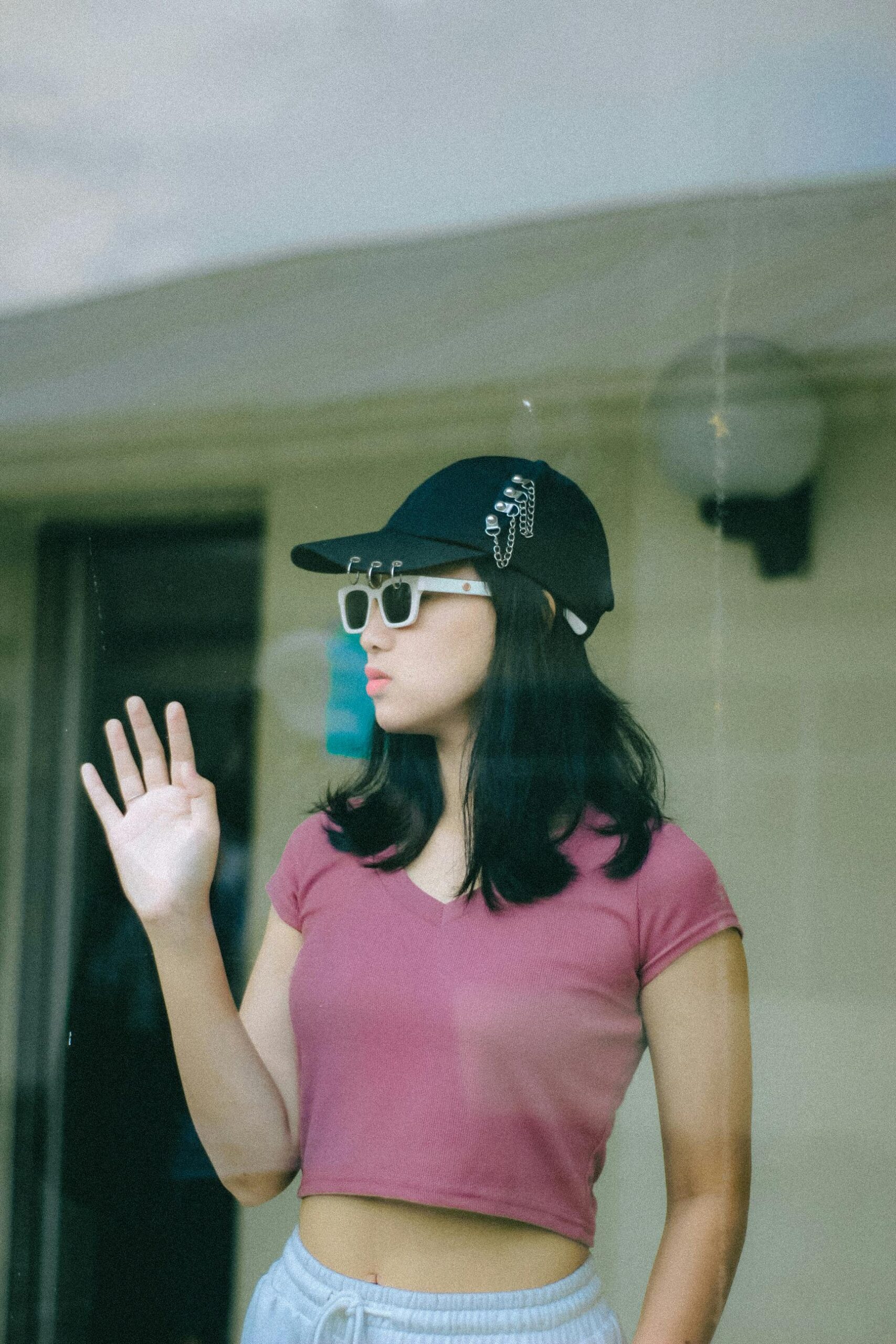 Young woman in casual attire and sunglasses waving indoors. Perfect for fashion and lifestyle themes.