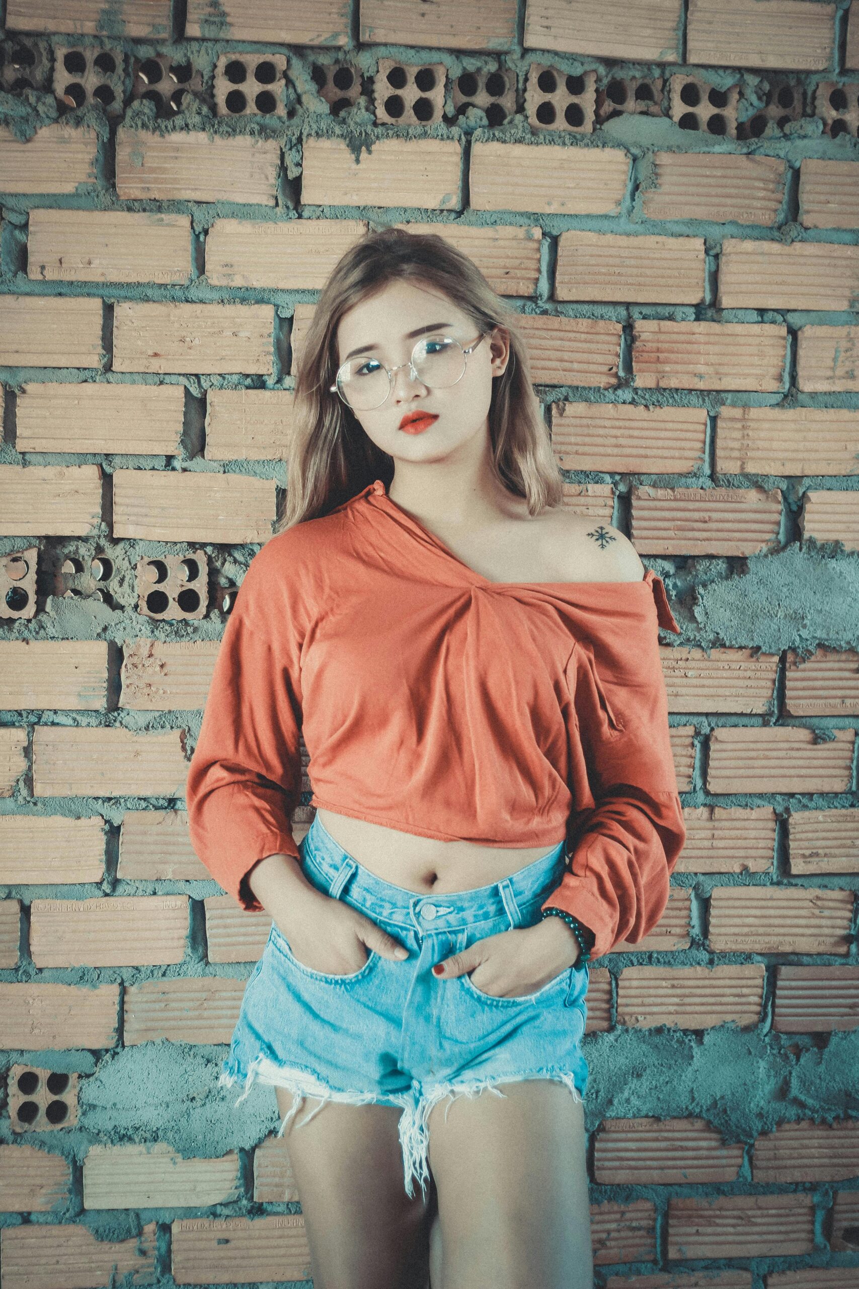Fashionable woman in casual clothes posing against a brick wall.